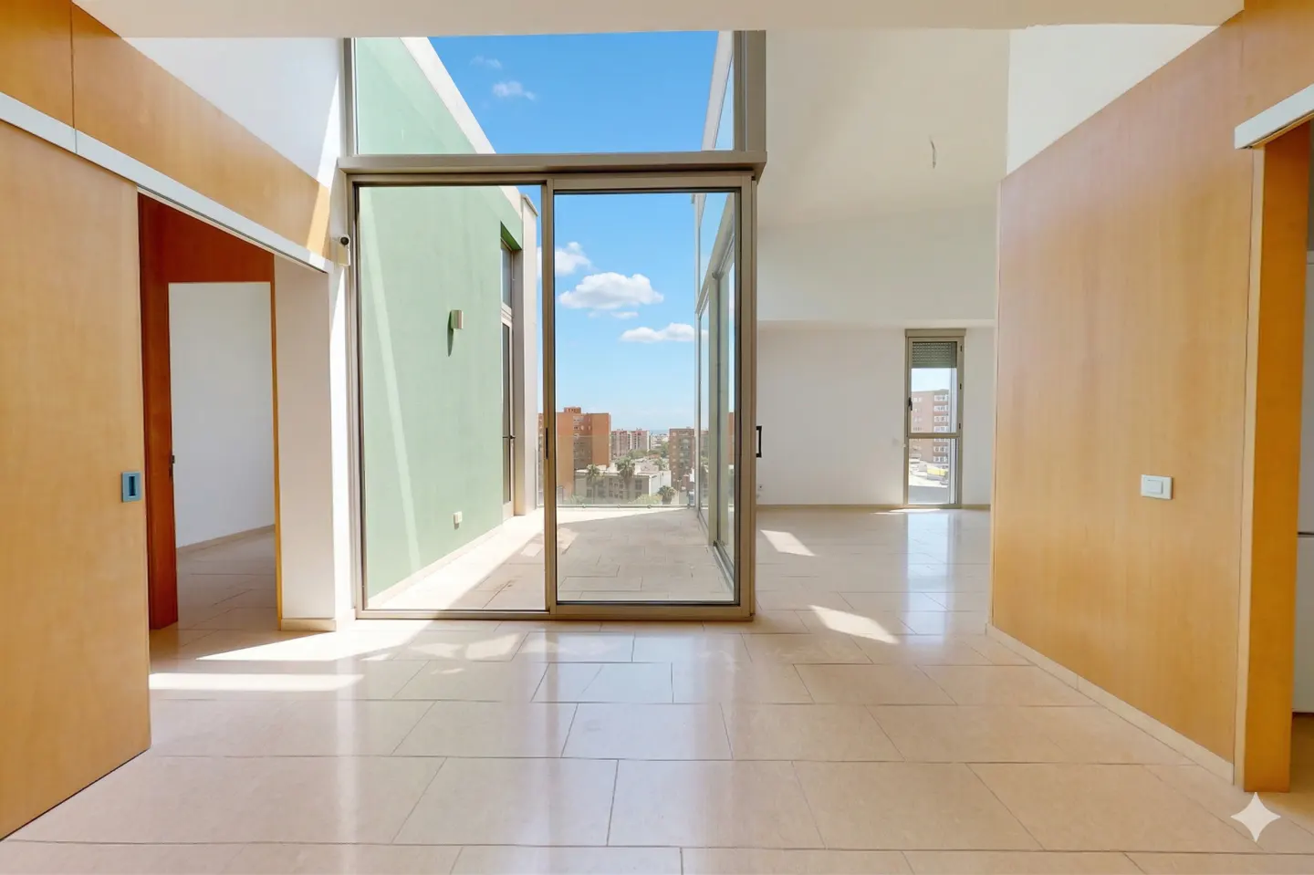 Modern apartment interior with light tile floors, wood-paneled walls, and large sliding glass doors opening to a balcony.