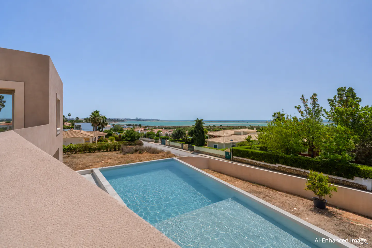A high-angle shot shows a rectangular pool with turquoise water, a beige building, and a distant ocean view under a clear blue sky.