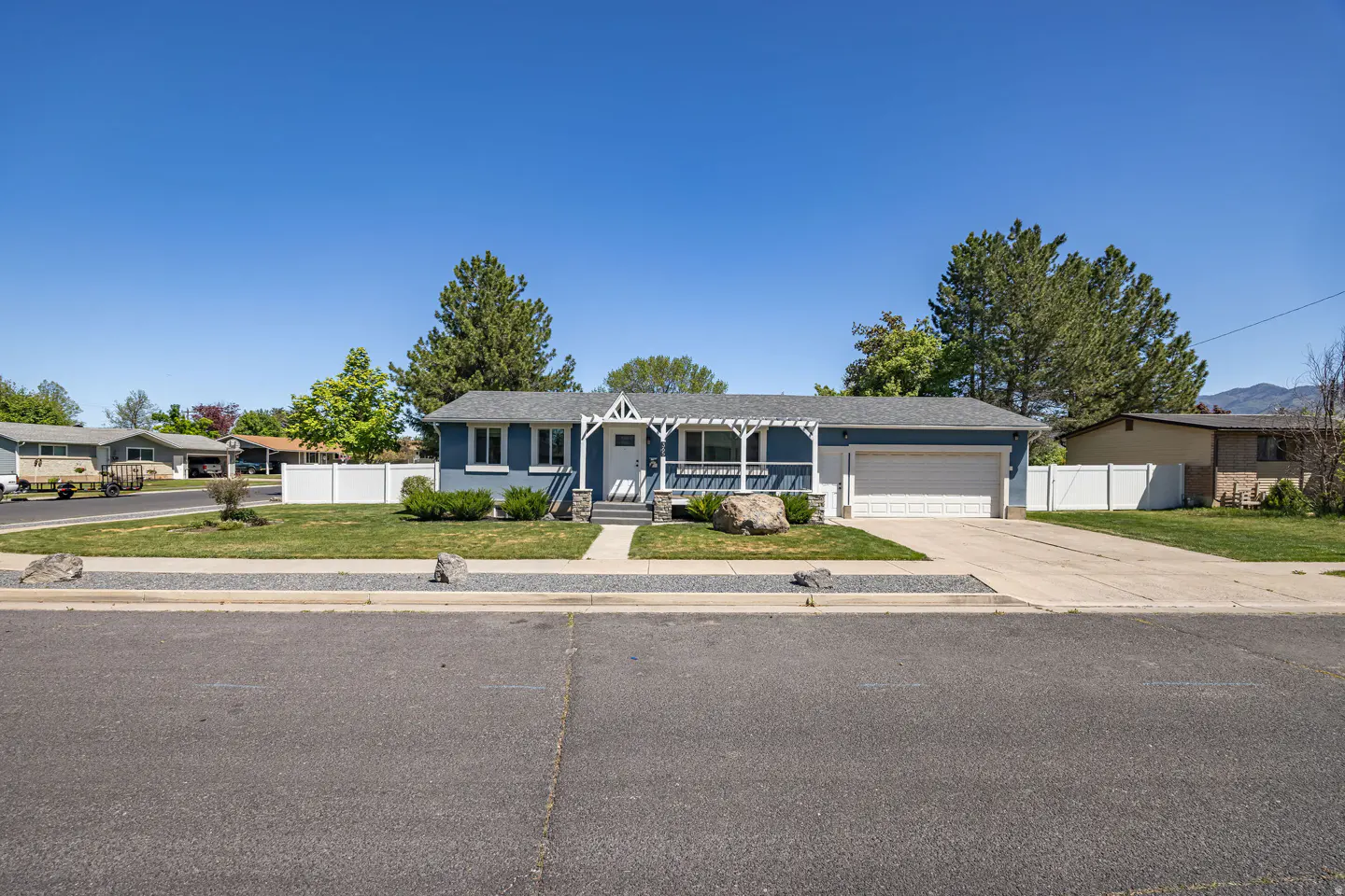 A blue single-story house with a white garage door and a white pergola over the front porch.