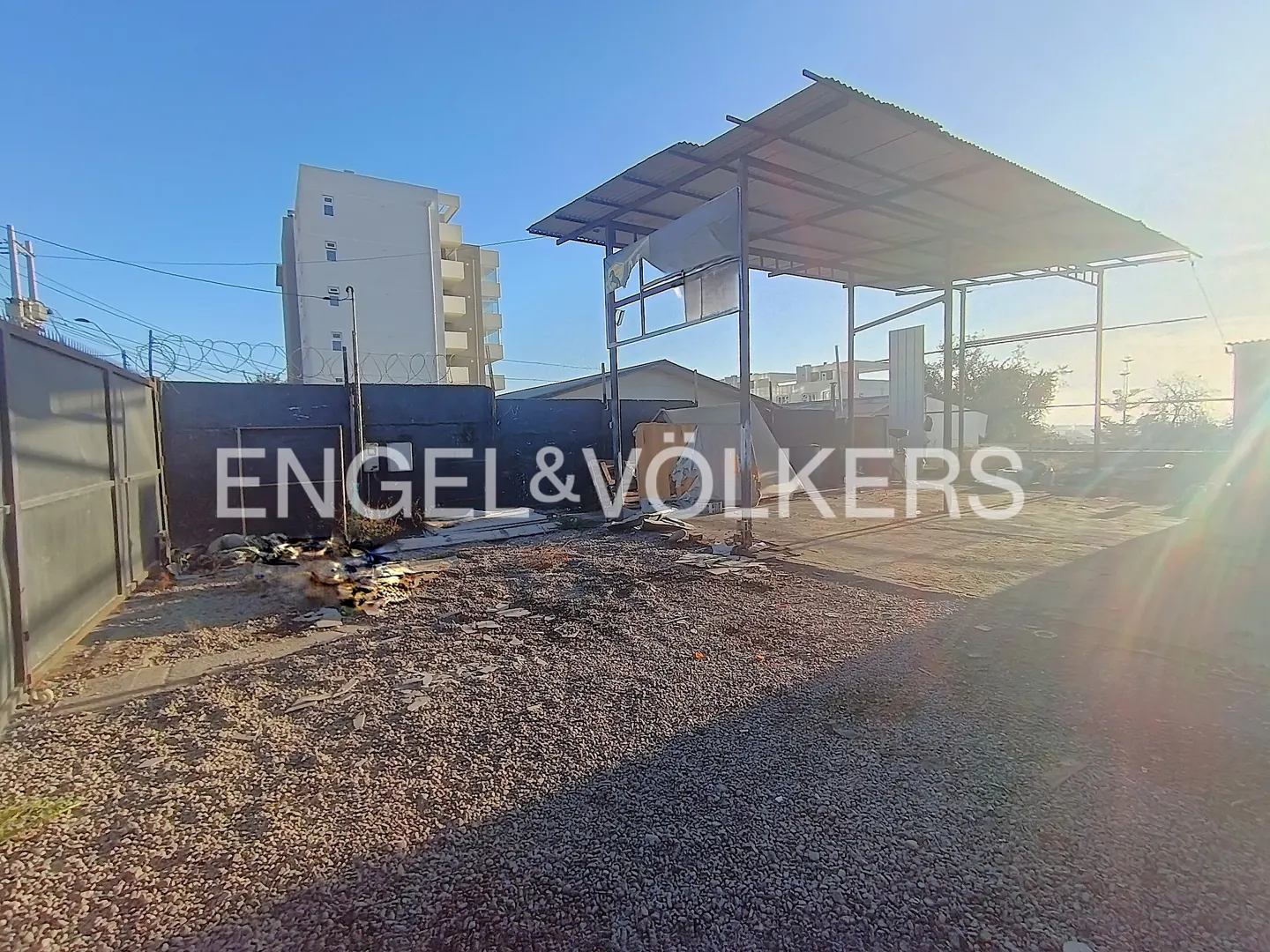 Outdoor shot of a gravel lot with a metal awning, a building in the background, and the Engel & Völkers logo.