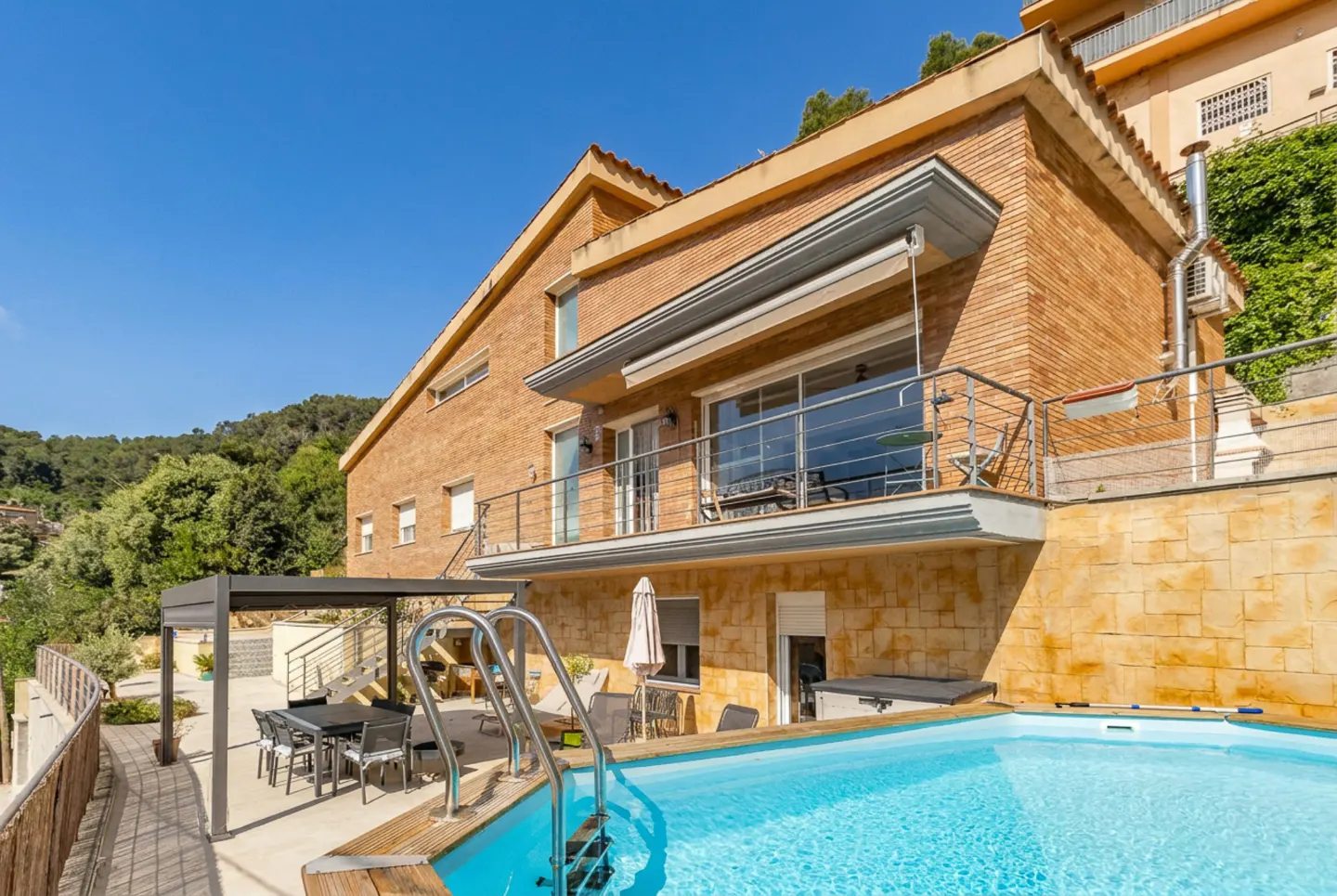 Exterior view of a two-story brick house with a blue swimming pool and patio furniture.