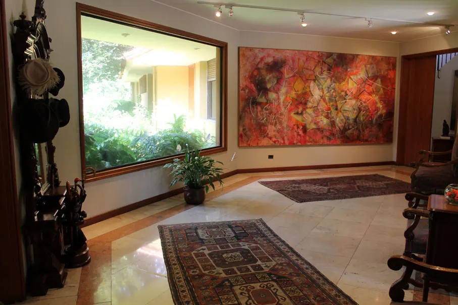 A foyer with marble floors, rugs, and a large window overlooking greenery. An abstract painting hangs on the wall.