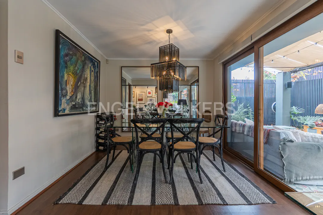 Dining room with a glass table, black chairs, a modern chandelier, and a large mirror, opening to a patio.