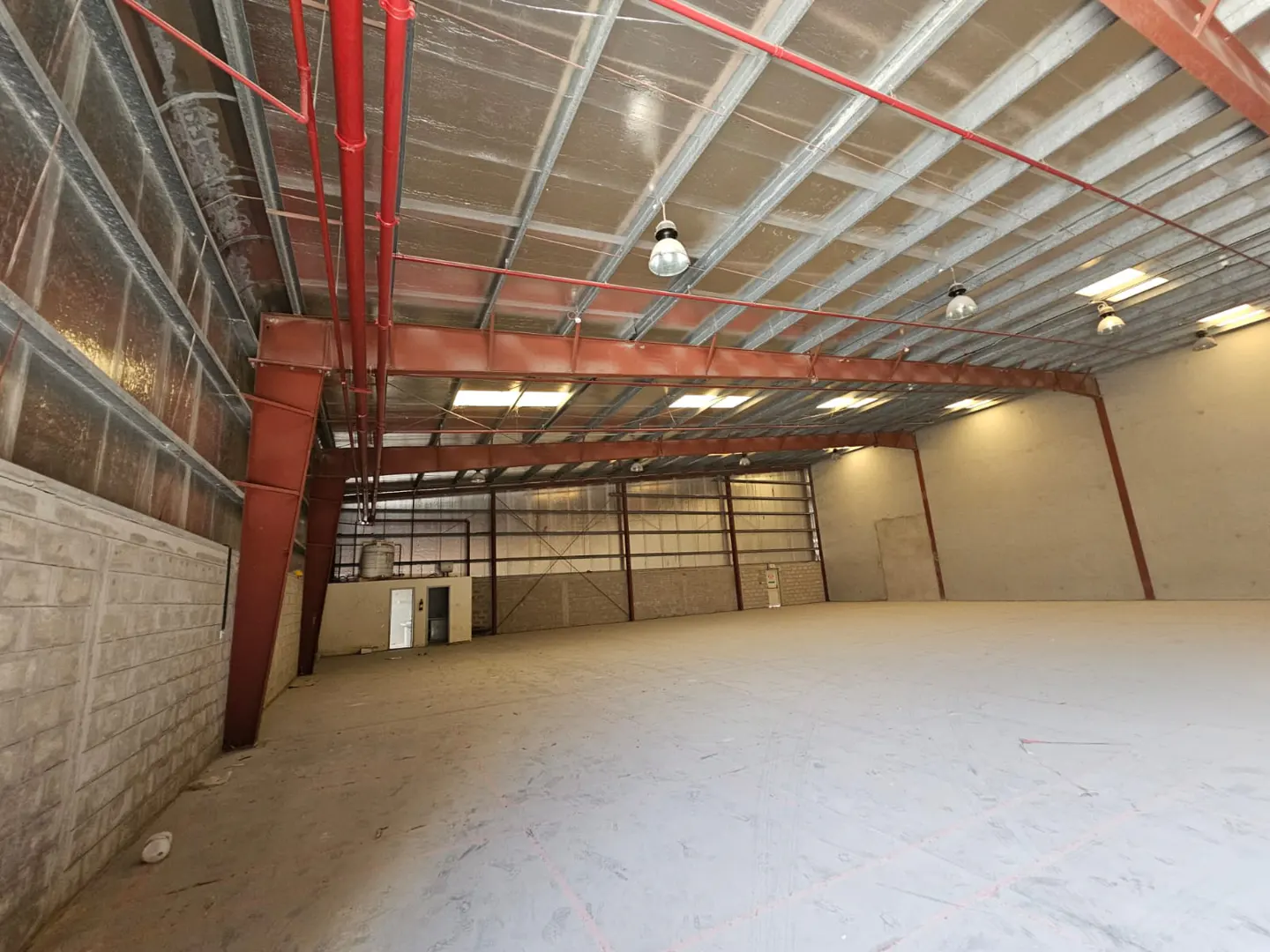 An empty warehouse with red support beams, a high ceiling, and concrete floors.