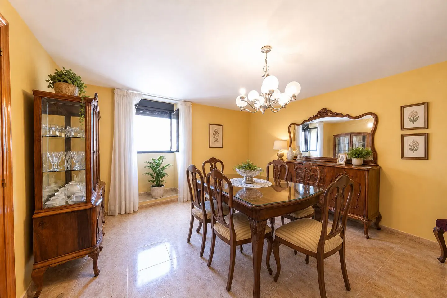A dining room with yellow walls, a glass-topped table, and a wooden china cabinet.