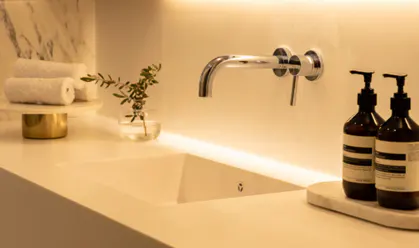 Modern bathroom sink with chrome faucet, two brown soap dispensers, and rolled white towels on a gold stand.