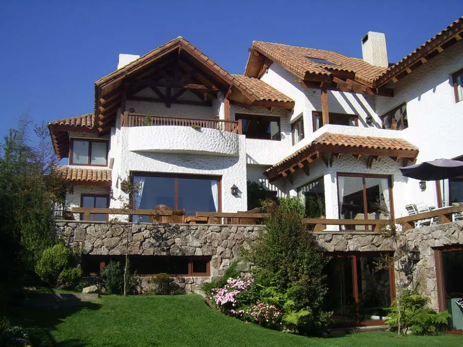 A large, white house with a brown tile roof sits on a stone foundation with a green lawn in front.