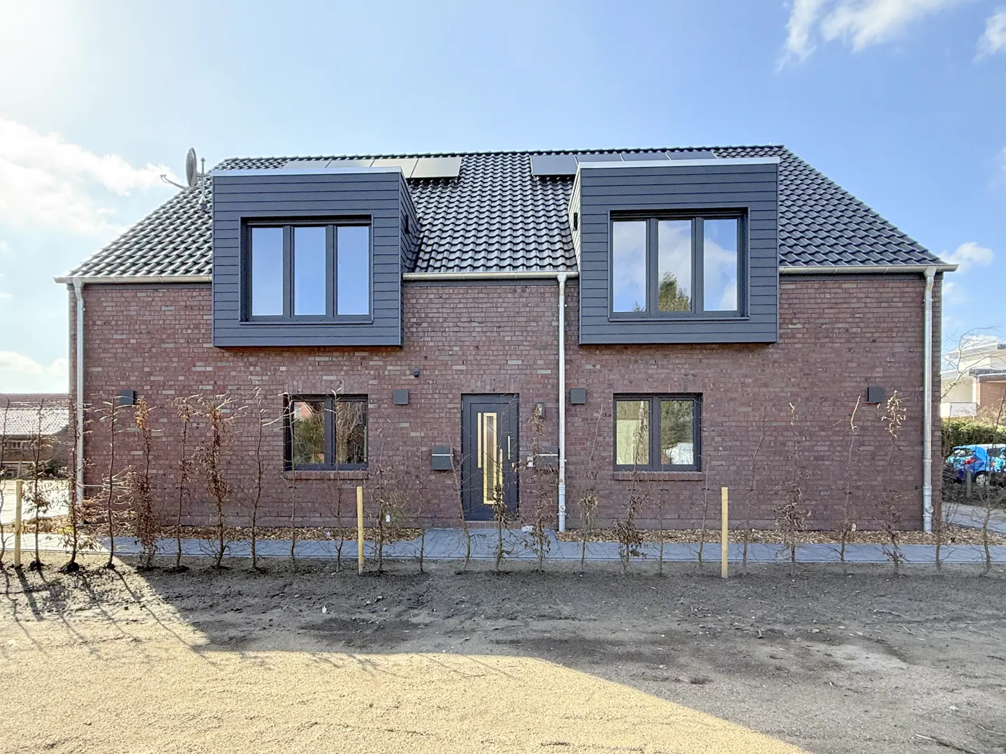 Two-story brick house with gray trim, dormer windows, and a dark gray tiled roof under a blue sky.
