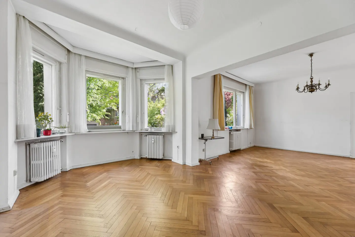 Bright, spacious living room with white walls, herringbone wood floors, large windows, and a classic chandelier.