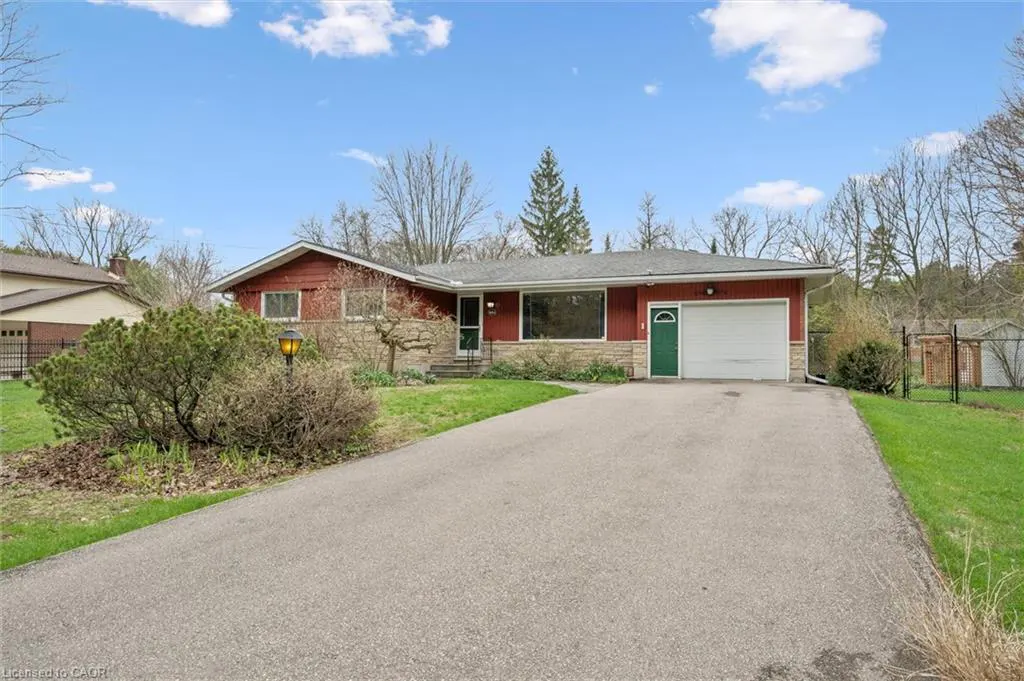 A single-story red house with a green door and a long driveway under a blue sky.