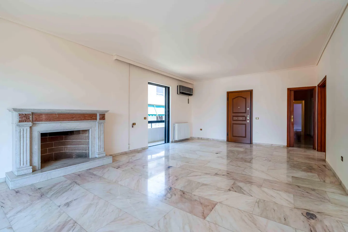Bright, empty living room with marble floors, a fireplace, and a door to a balcony.