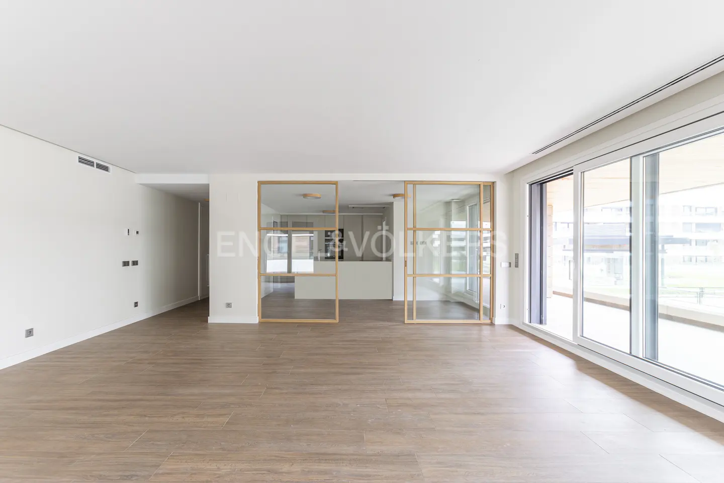 Bright, empty living room with wood-look tile floors, white walls, and glass sliding doors leading to a balcony.