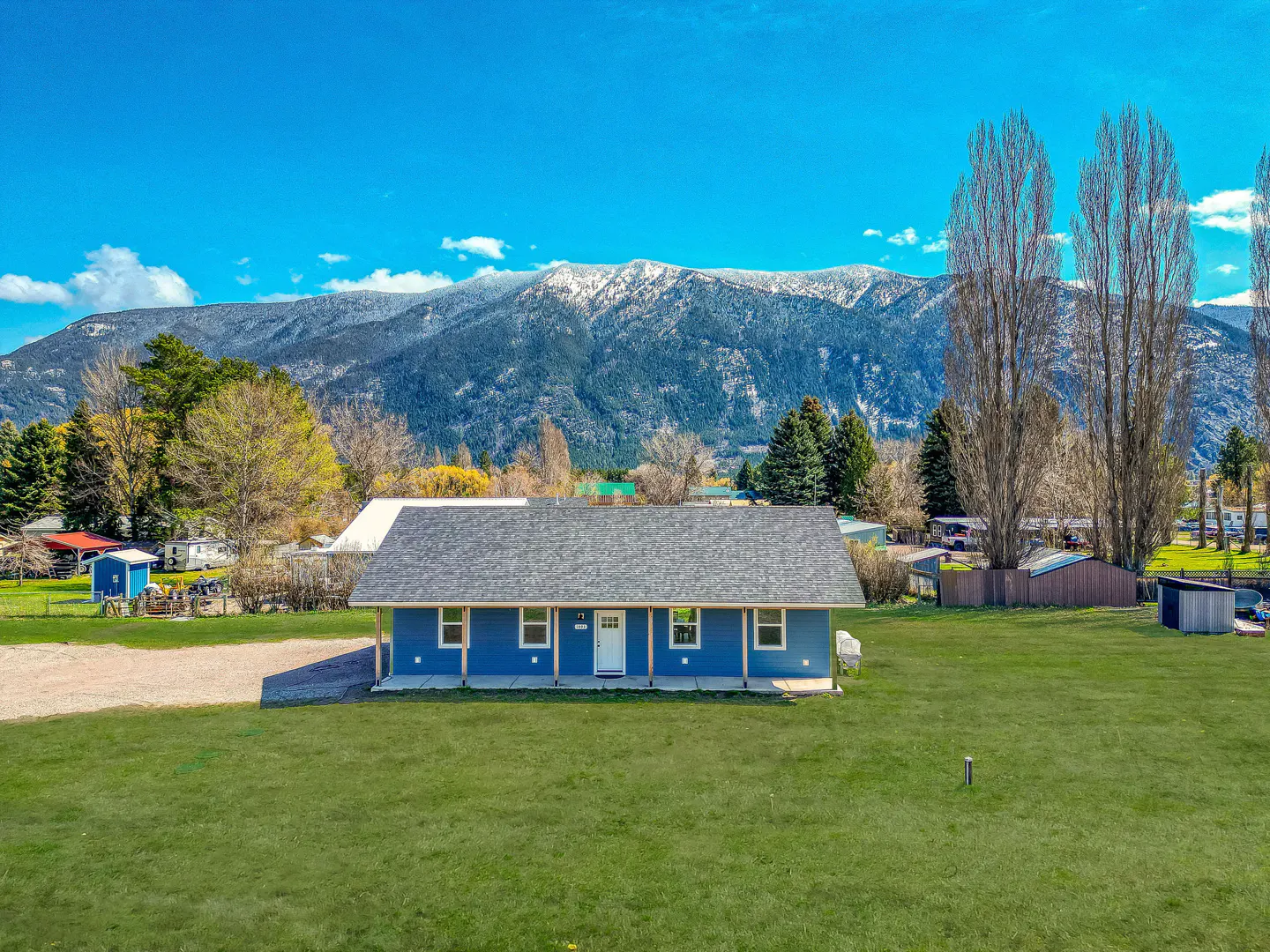 Blue single-story house with a gray roof and white trim, set against a backdrop of snow-capped mountains and a clear blue sky.