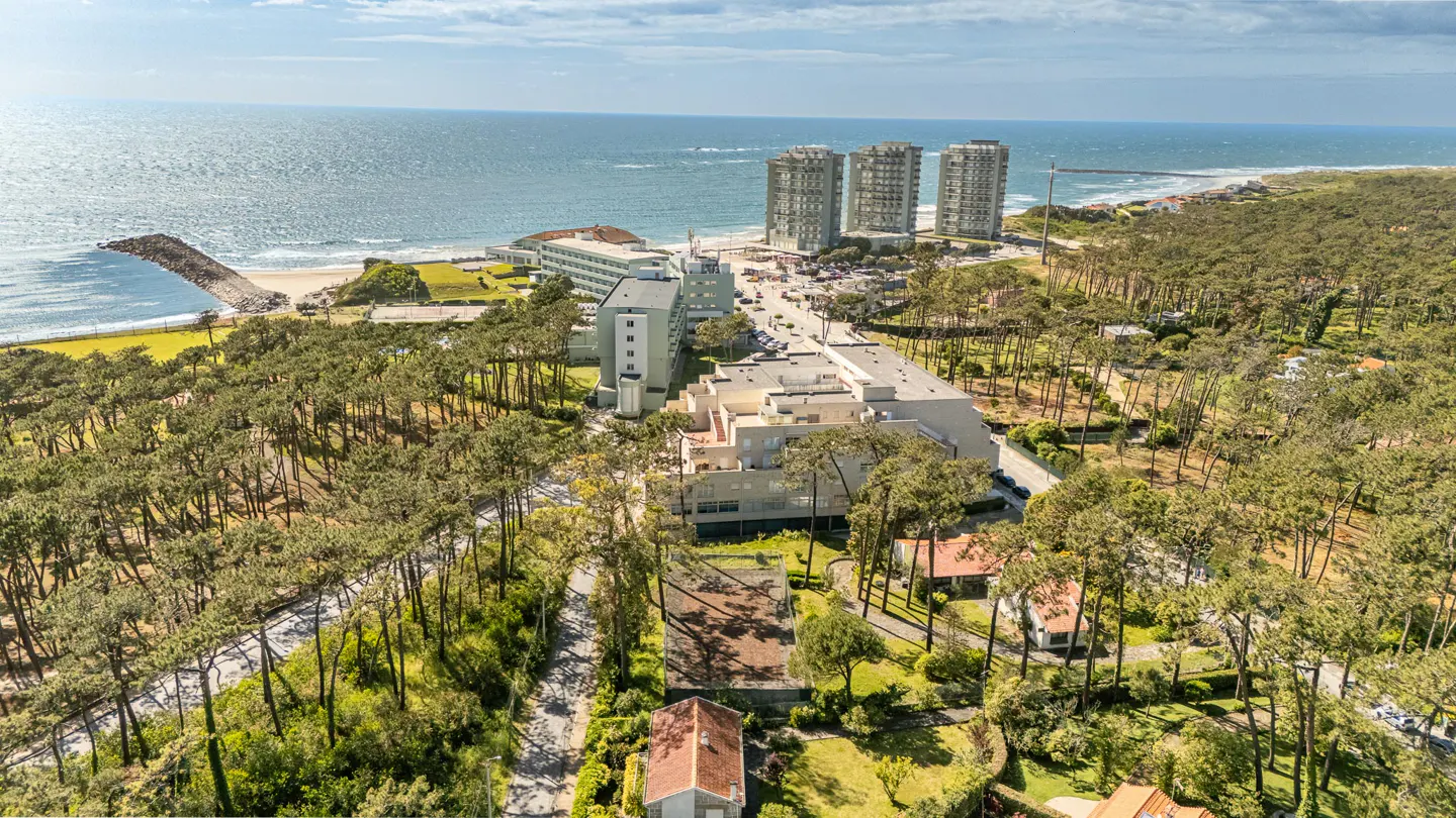 Aerial view of a coastal resort with tall buildings, a hotel, and lush green trees near the ocean.