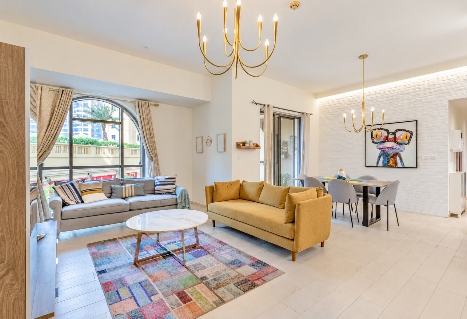 Bright living room with a mustard sofa, grey couch, marble coffee table, colorful patchwork rug, and dining area. [AI-generated text]