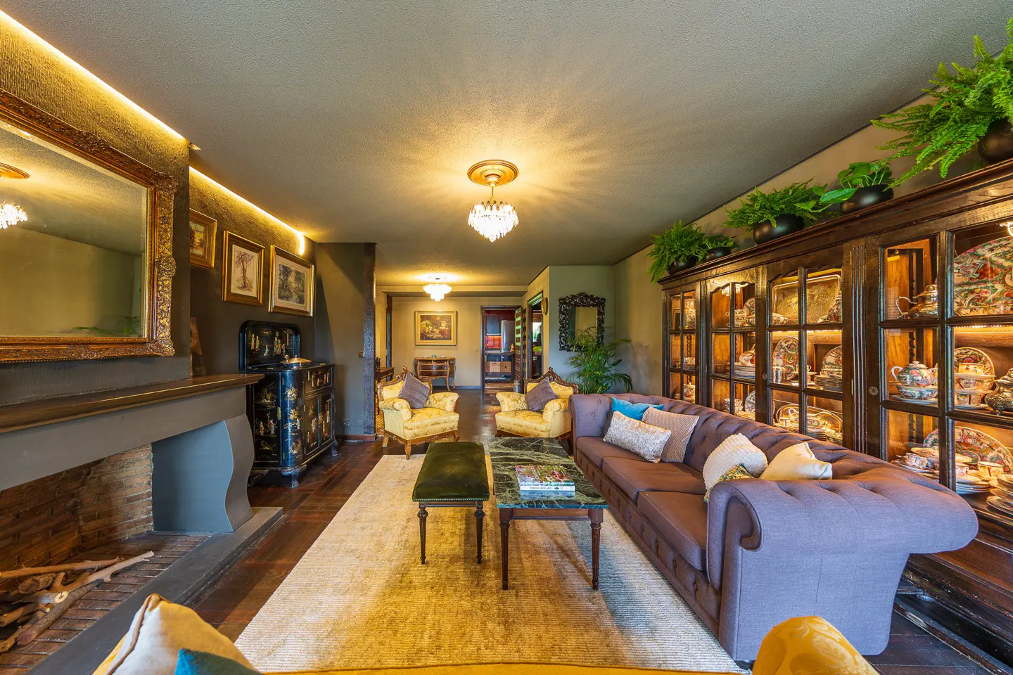 A living room with a fireplace, a purple sofa, yellow armchairs, and a dark wood cabinet with plants on top.