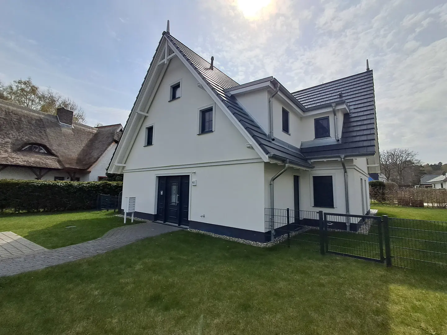 Two-story white house with a dark roof and black trim, surrounded by green grass and a gray stone walkway.