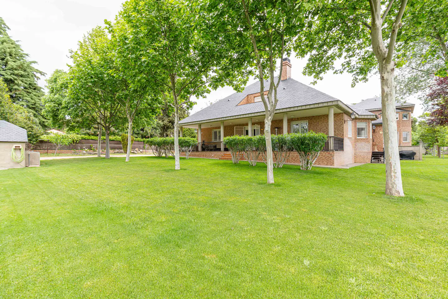 Brick house with a gray roof and a long porch, surrounded by green trees and a large green lawn.