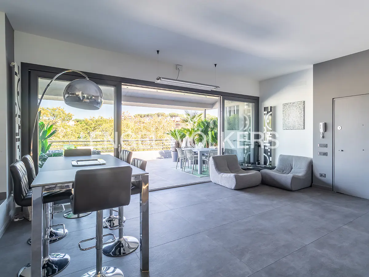A modern, gray living room with a dining table, bar stools, and a sliding glass door to a patio.