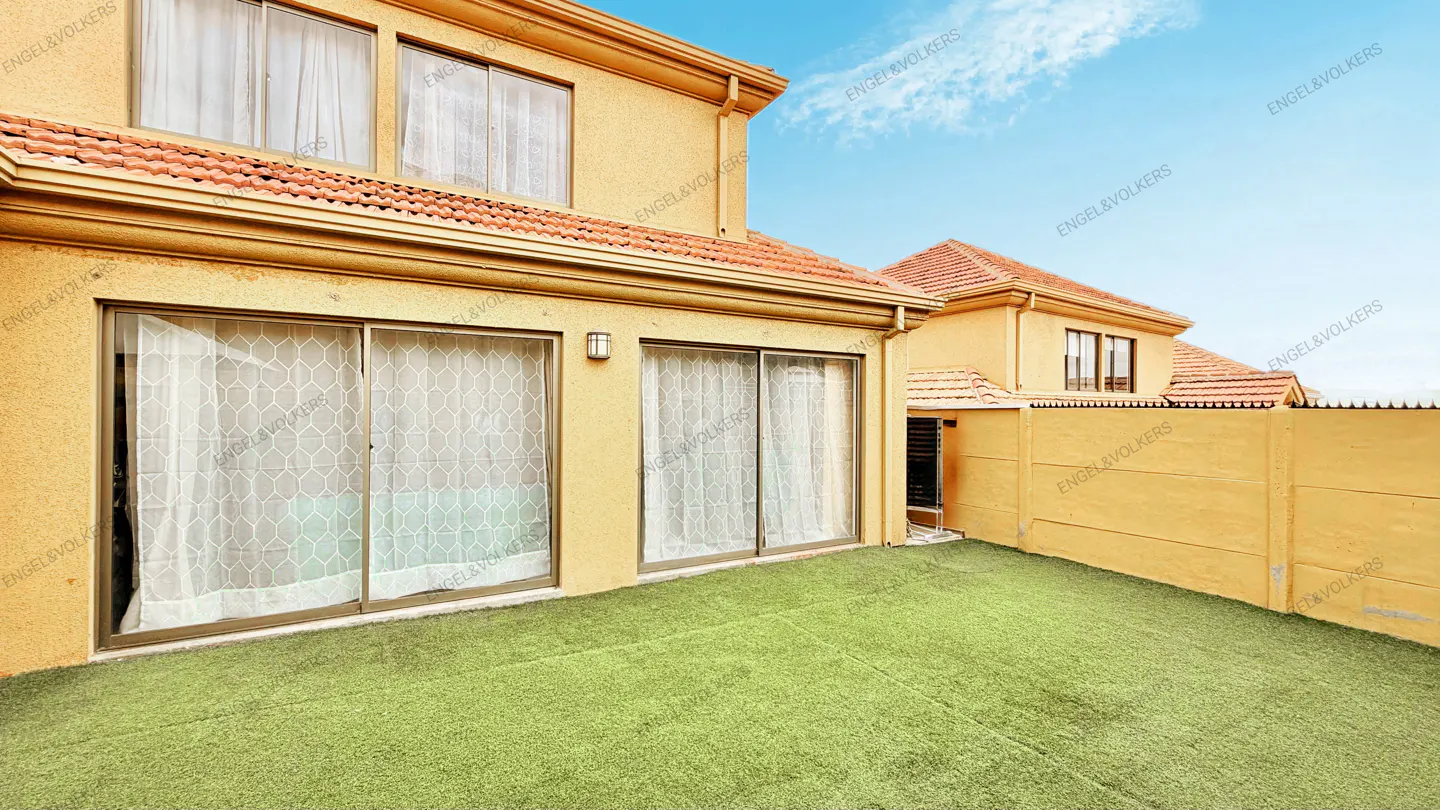 Exterior view of a yellow house with a red tile roof and a green lawn. Sliding glass doors with white curtains are visible.