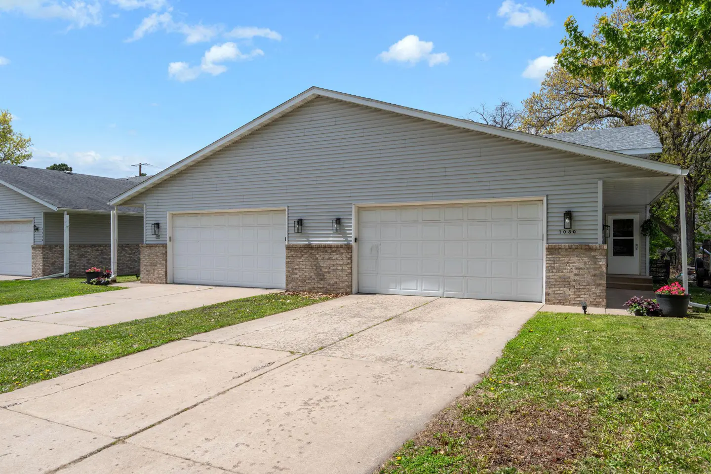 Exterior of a light gray duplex with white garage doors and a concrete driveway.
