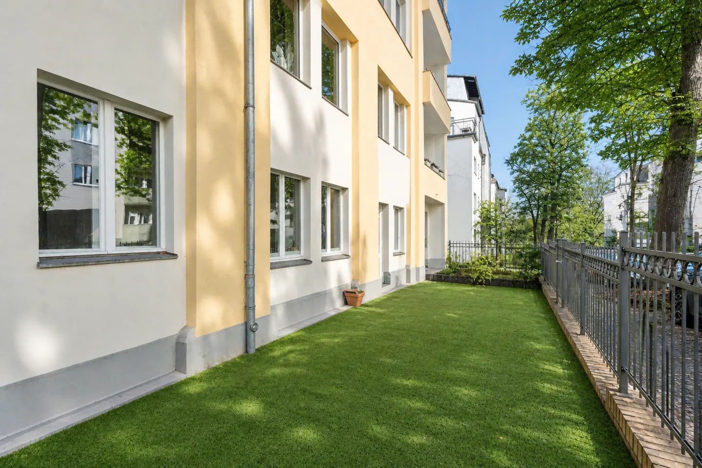 Exterior view of a yellow and white apartment building with a green lawn and black metal fence.