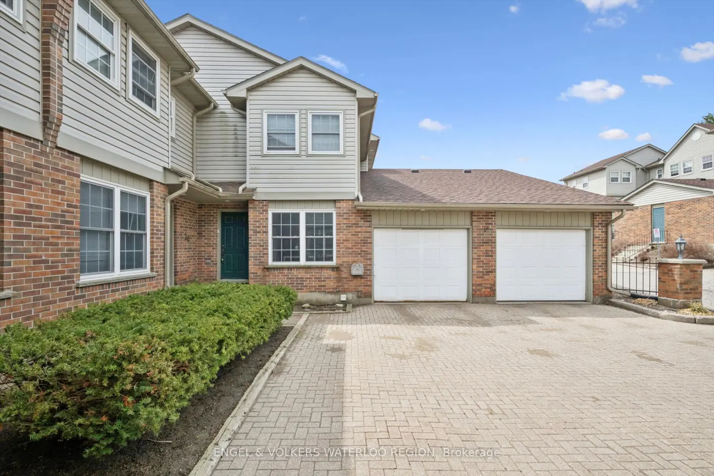 Exterior of a two-story townhouse with brick and siding, a green door, and a two-car garage under a blue sky.