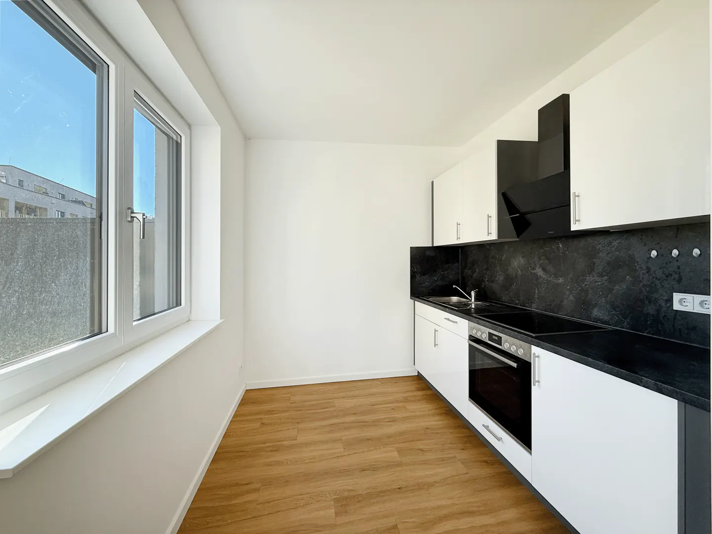Bright kitchen with white cabinets, black countertops and backsplash, and wood-look flooring. A window provides natural light.
