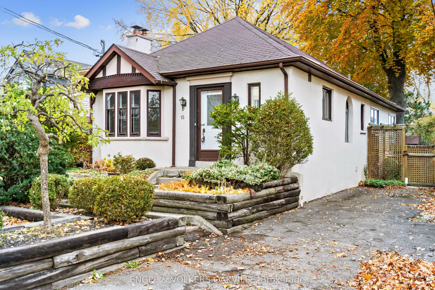 A white, one-story house with brown trim and a brown roof, surrounded by trees with yellow leaves.