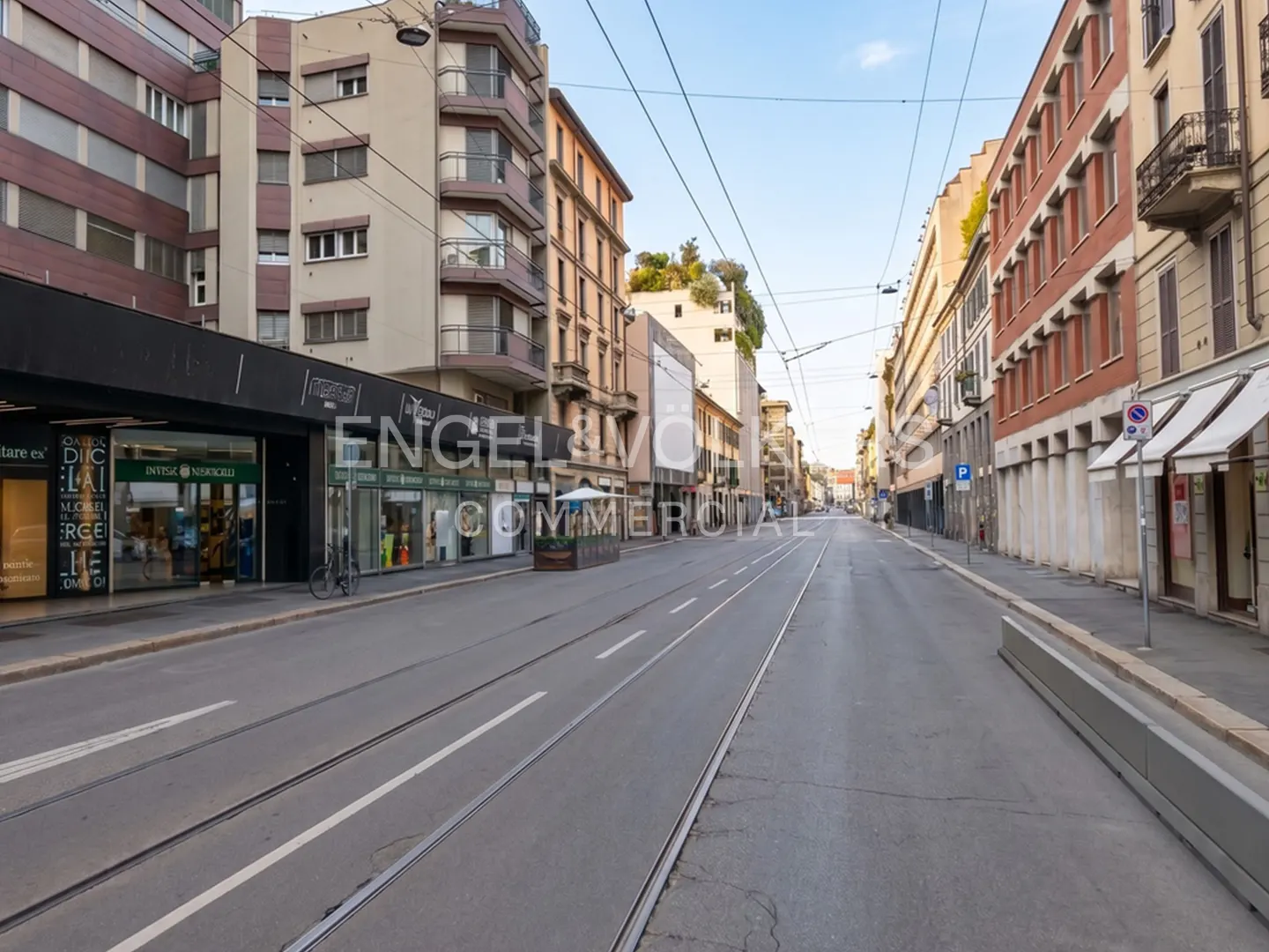 Street view of a commercial district with buildings, shops, and tram tracks running down the center of the road.