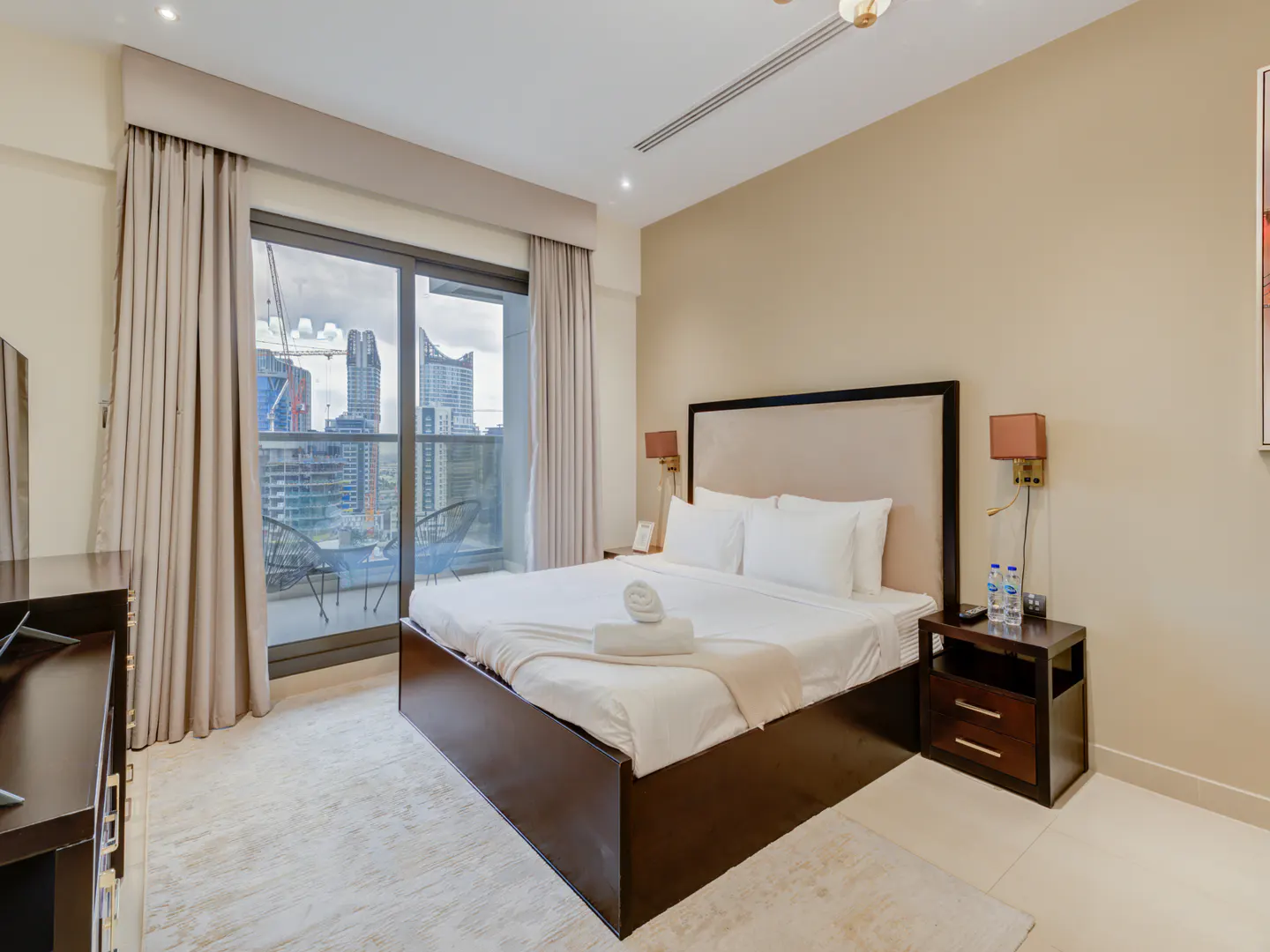 Bedroom with a king bed, white linens, and a city view from the balcony. Neutral tones and modern decor create a relaxing atmosphere.