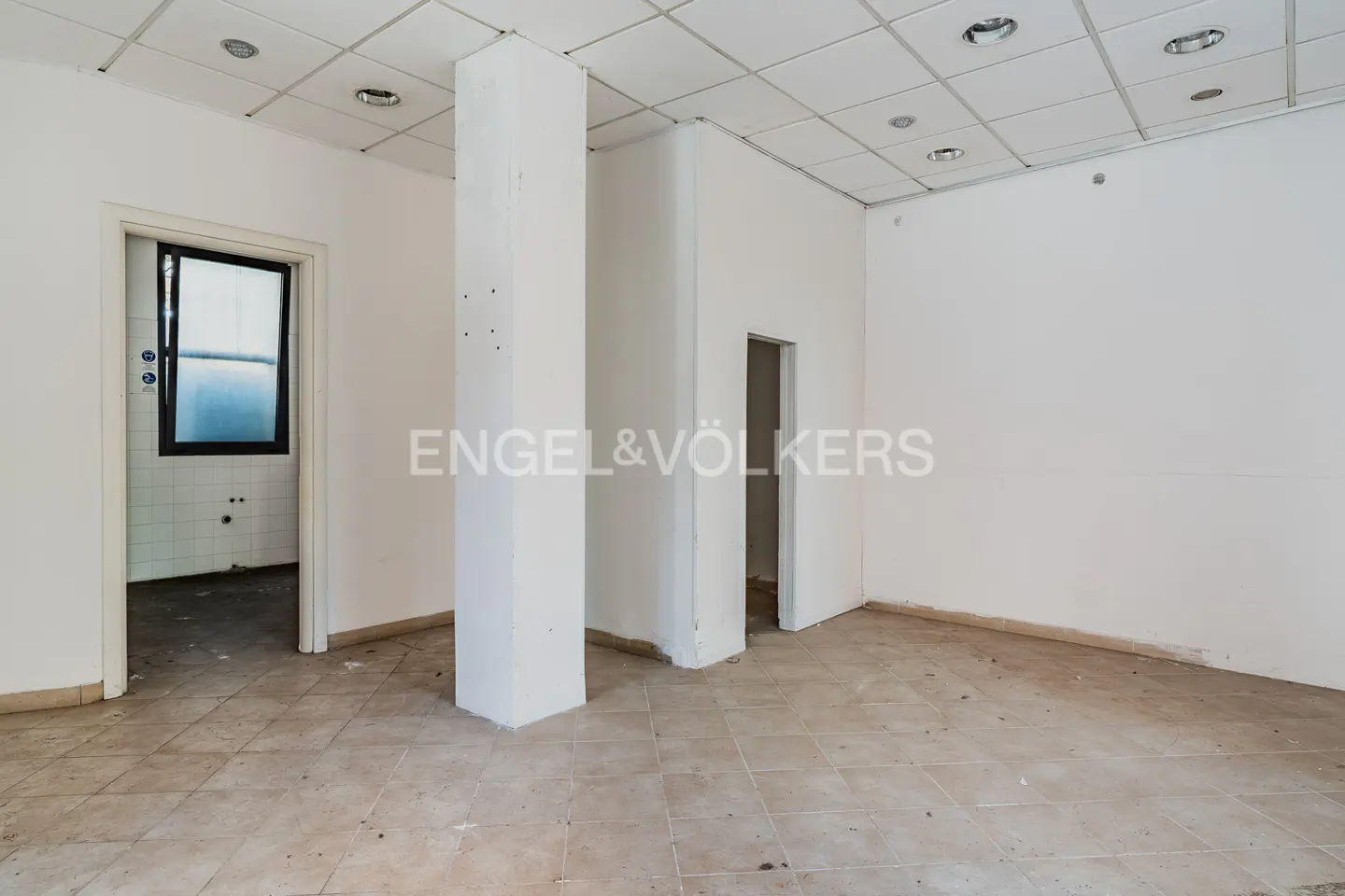 Empty white room with tile floor, white walls, and two white support columns. A doorway leads to a room with a black-framed window.
