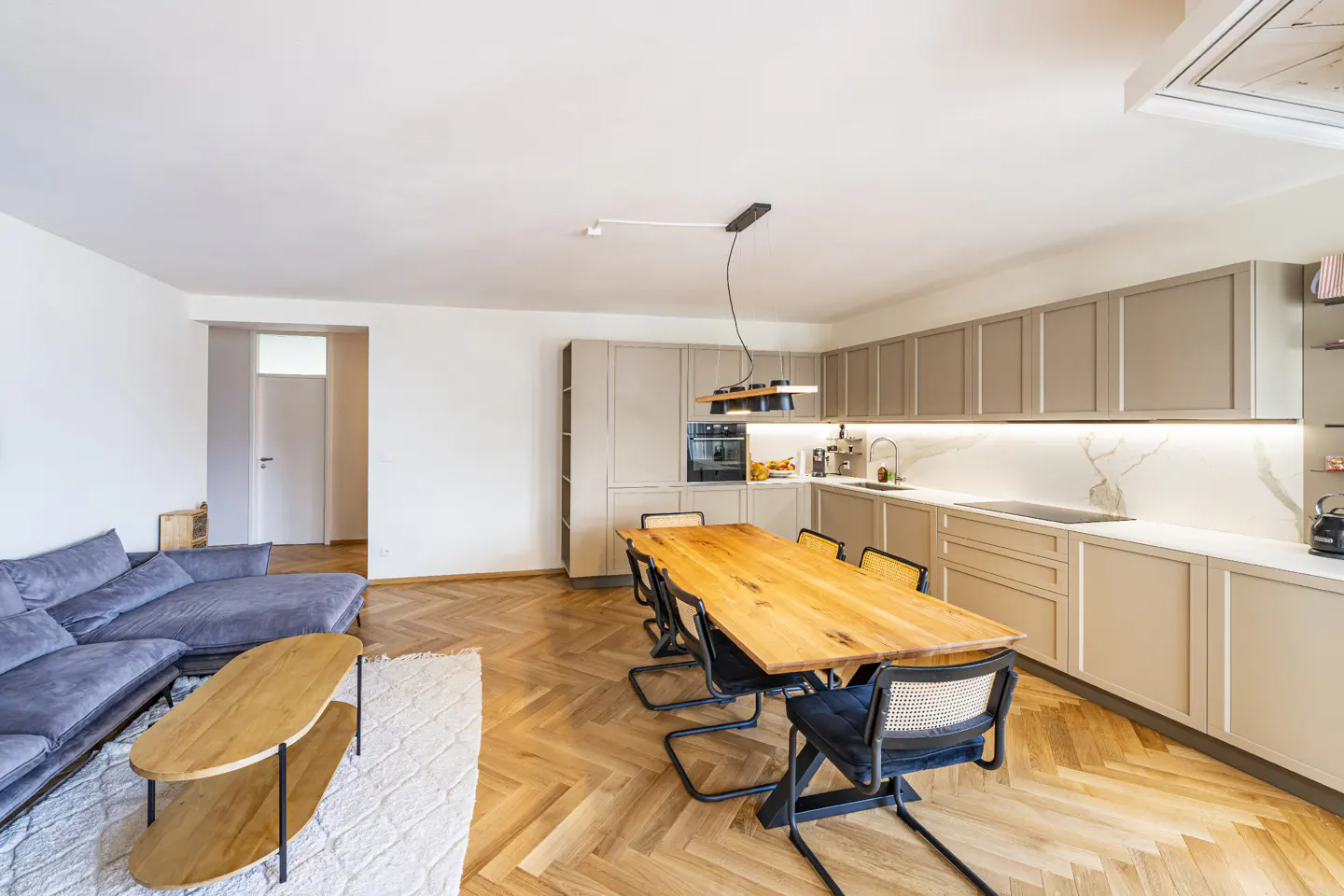 Open-concept living space with a gray sofa, wood table, and kitchen with gray cabinets and marble countertops.