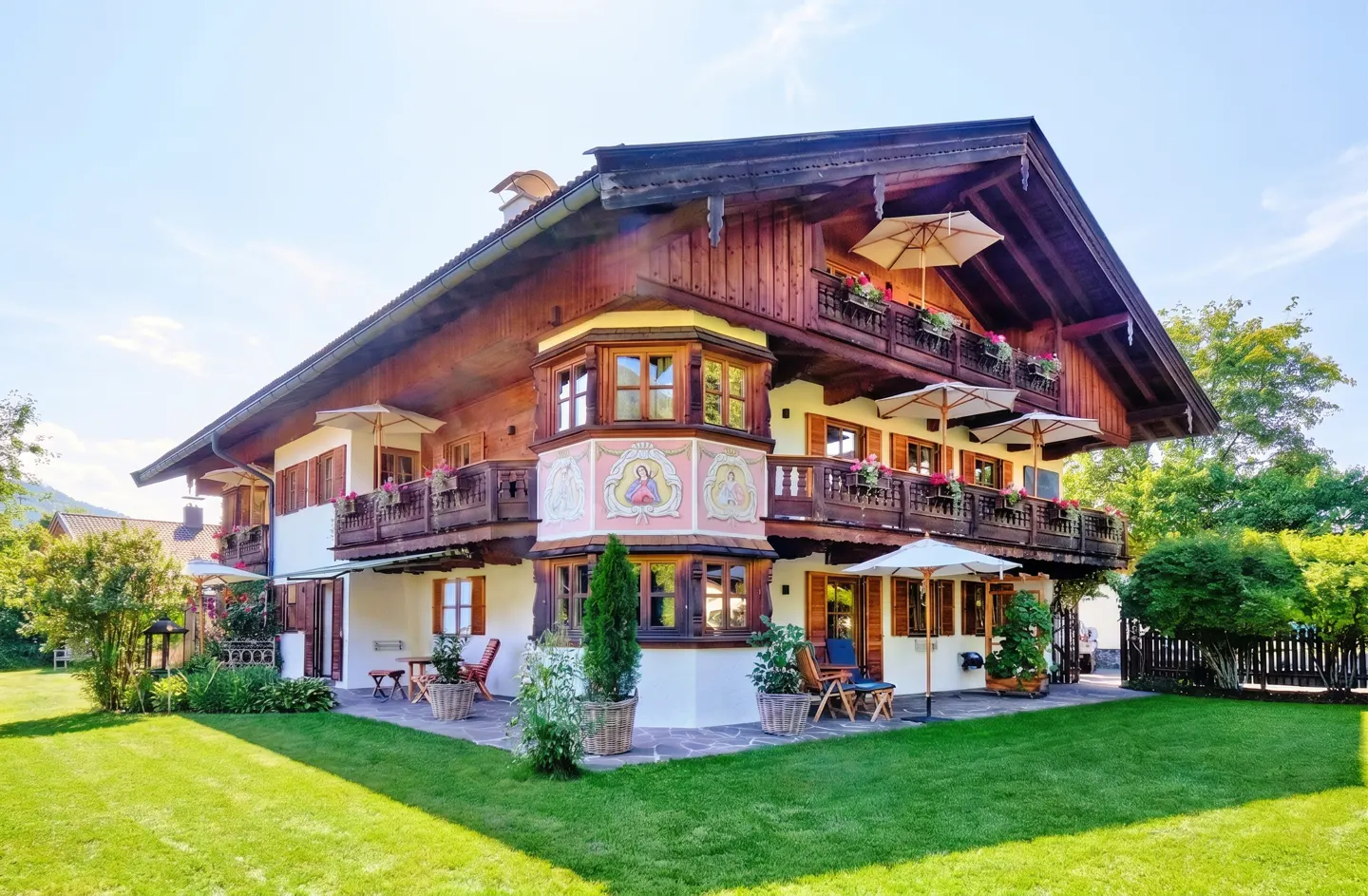 A three-story chalet-style house with brown wood and white walls, balconies, and a green lawn.
