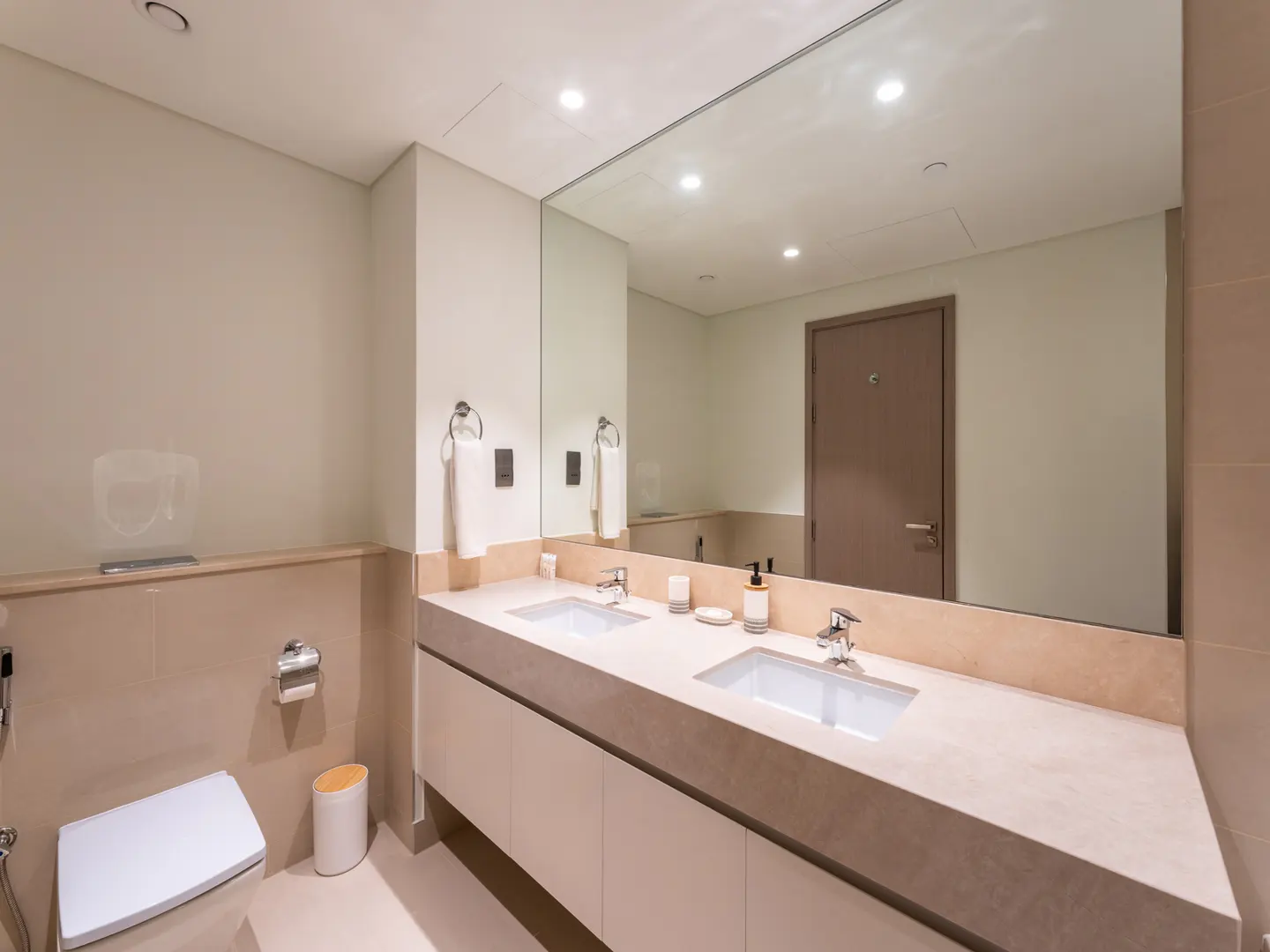 Modern bathroom with double sink vanity, large mirror, and toilet. Neutral color palette.
