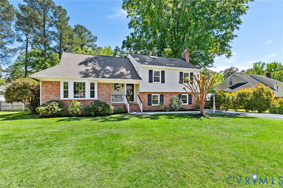 Two-story house with brick and white siding, black shutters, and a green lawn on a sunny day.