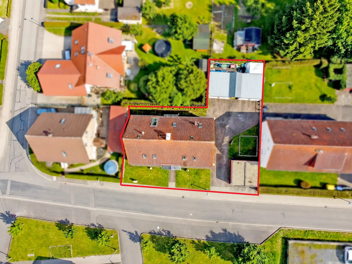 Aerial view of a house with a red roof, surrounded by a red boundary line, with a green lawn and trees.