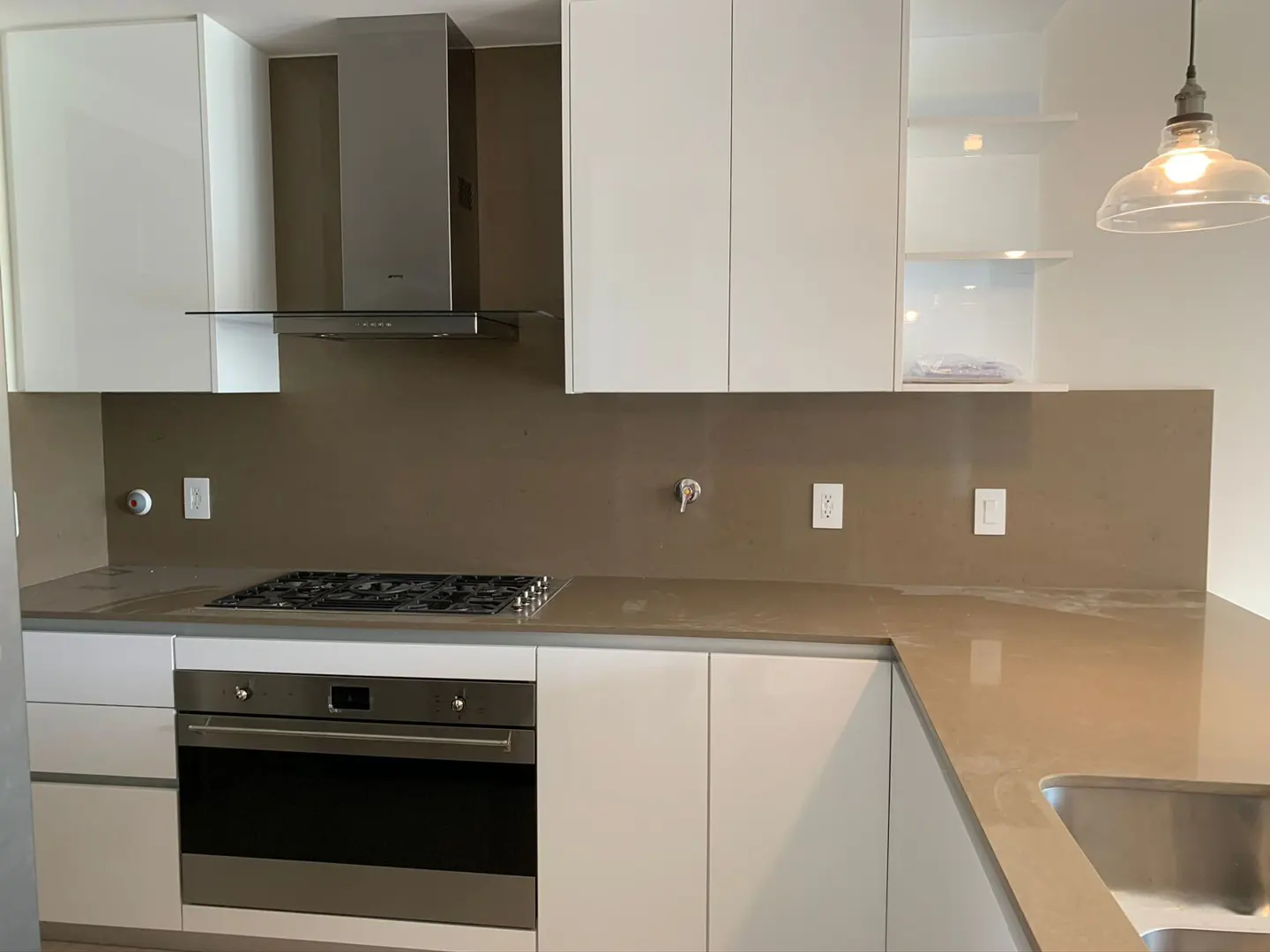 Modern kitchen with white cabinets, stainless steel appliances, and a brown backsplash. A clear glass pendant light hangs above the sink.