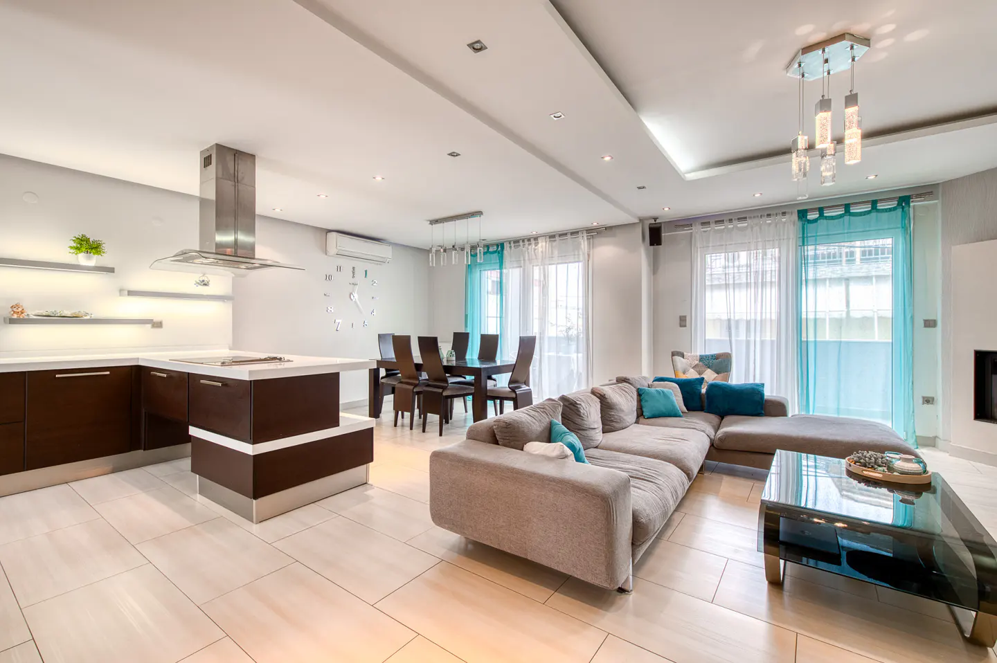 Open-concept living space with a brown kitchen island, dining table, and a gray sectional sofa with blue pillows.