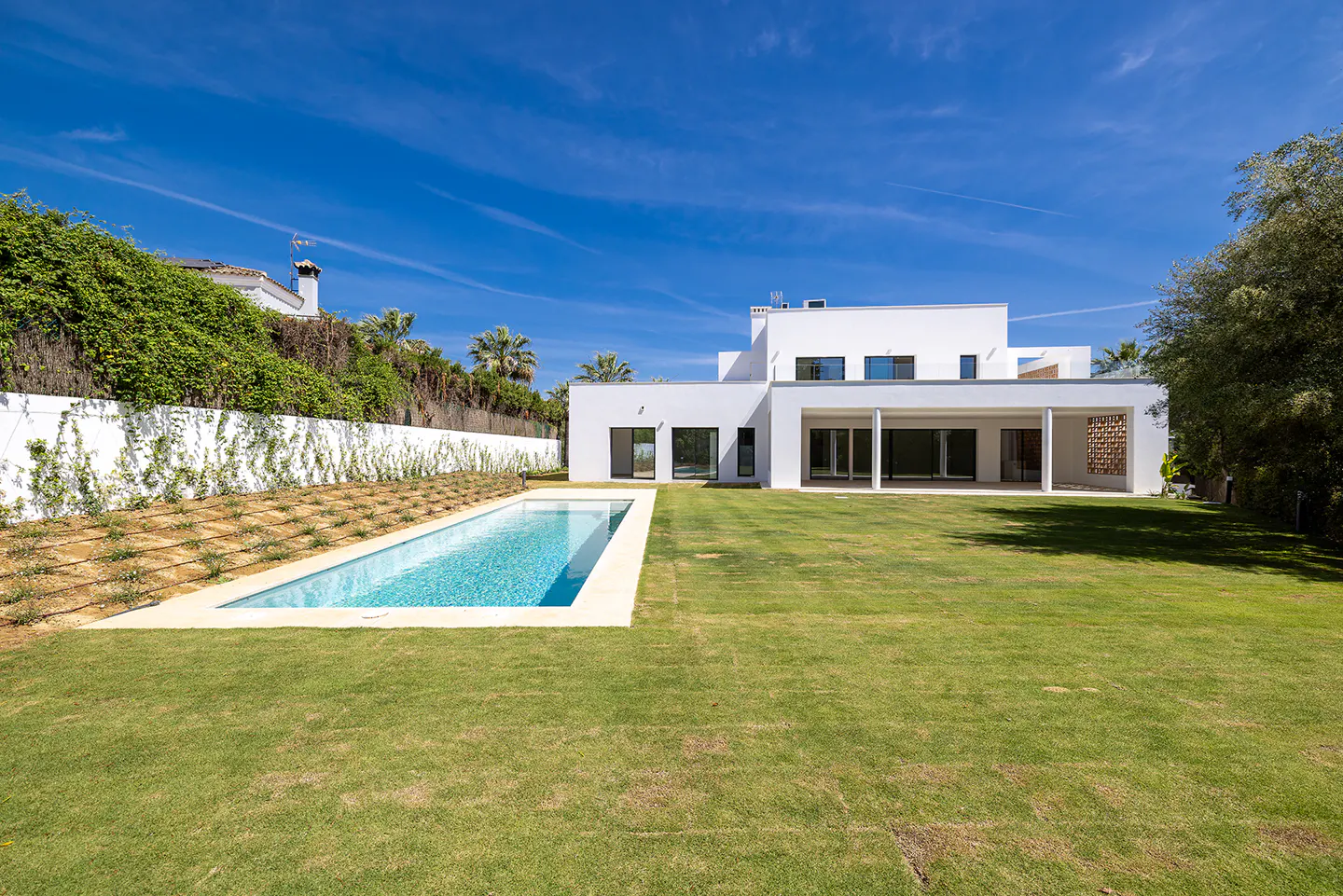 A modern white house with a pool and green lawn under a blue sky.