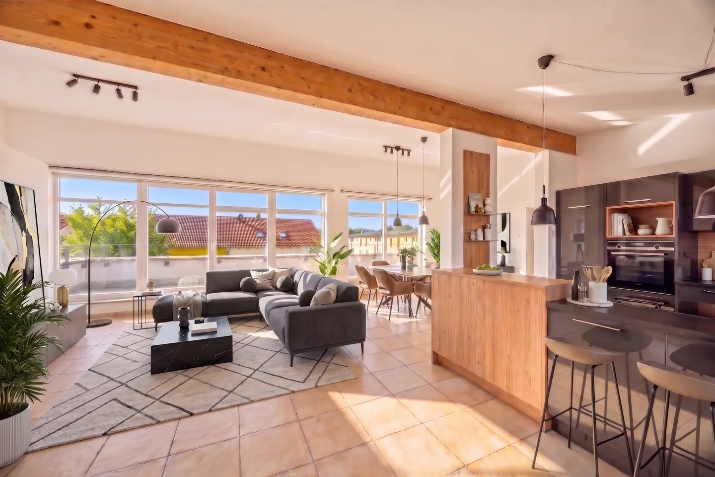 Open-concept living space with a gray sofa, black coffee table, and a kitchen island with bar stools. Large windows offer natural light.