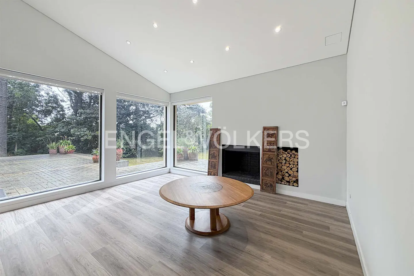 Modern living room with light wood floors, a round wooden table, and a fireplace with stacked logs and decorative screens.