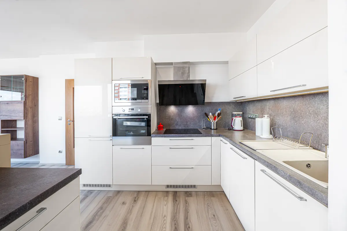 Modern kitchen with white cabinets, stainless steel appliances, grey countertops, and light wood-look flooring.