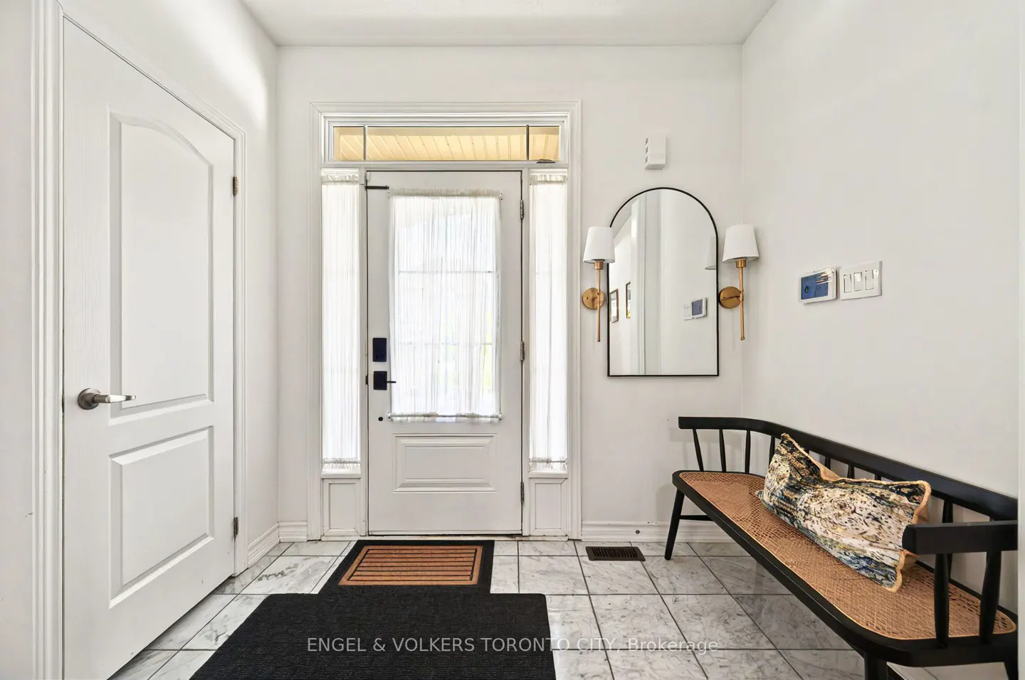 Bright entryway with white walls, marble floors, and a black bench with a patterned pillow. A white door with sheer curtains is centered.