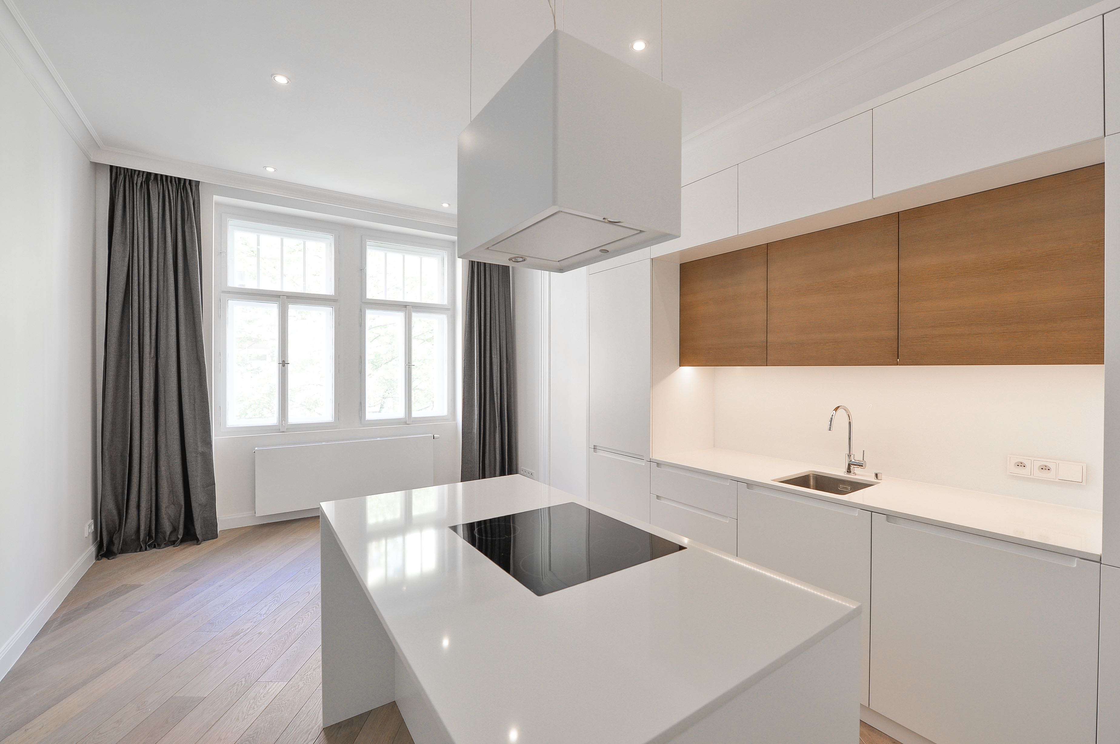 Modern white kitchen with a central island, wood-toned cabinets, and large windows with grey curtains. [AI-generated text]