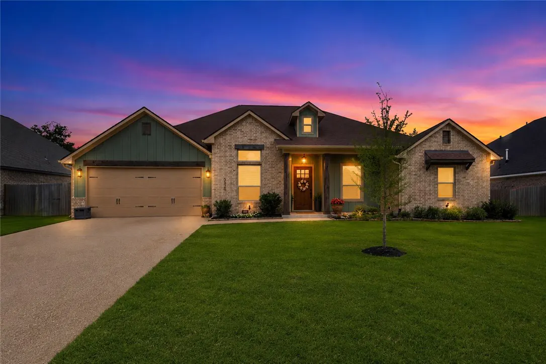 A single-story brick home with a green garage door and a manicured lawn at dusk.
