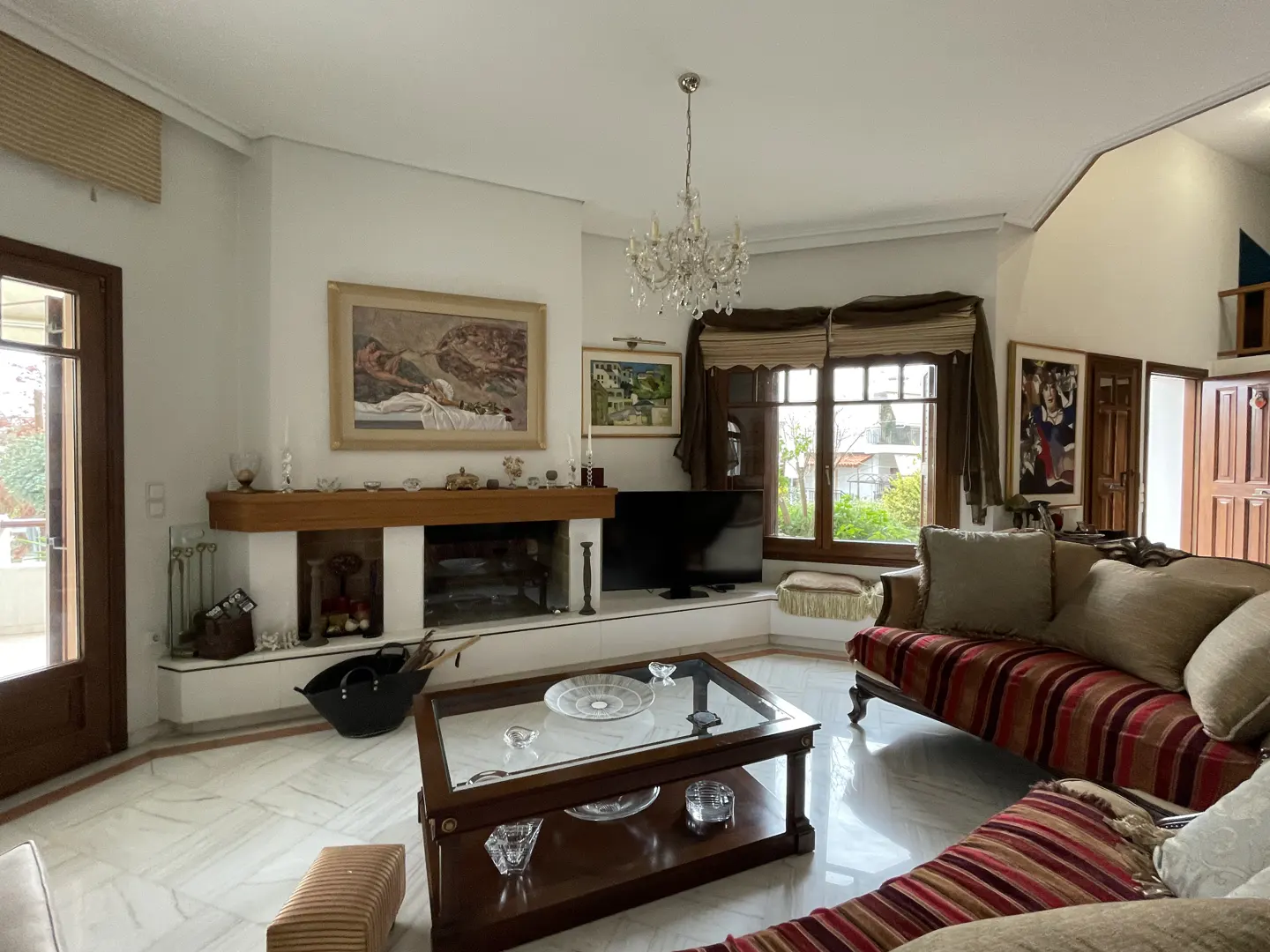 Living room with marble floors, a fireplace, a glass-top coffee table, and a striped sofa under a crystal chandelier.