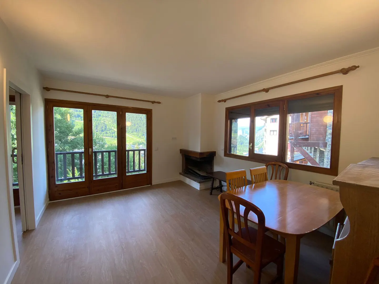 Living room with wood floors, fireplace, dining table, and balcony doors with a view of green trees.