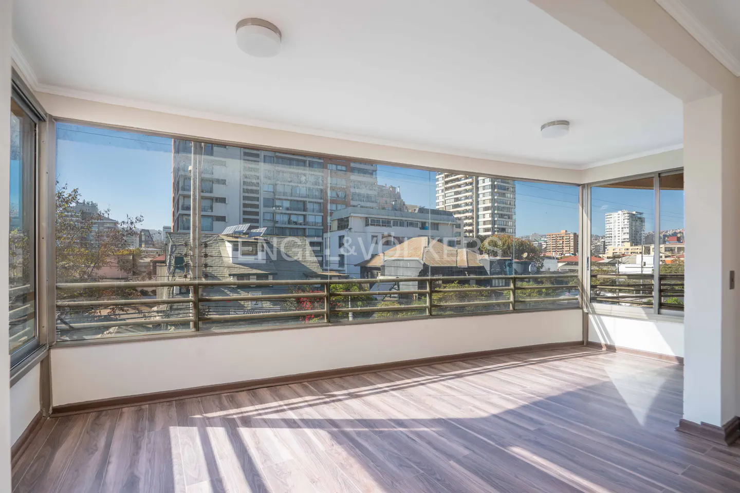 Bright, empty room with wood floors and floor-to-ceiling windows showing a city view.