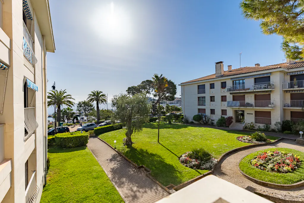 View from a balcony overlooking a green lawn with flowers, palm trees, and buildings under a bright blue sky.